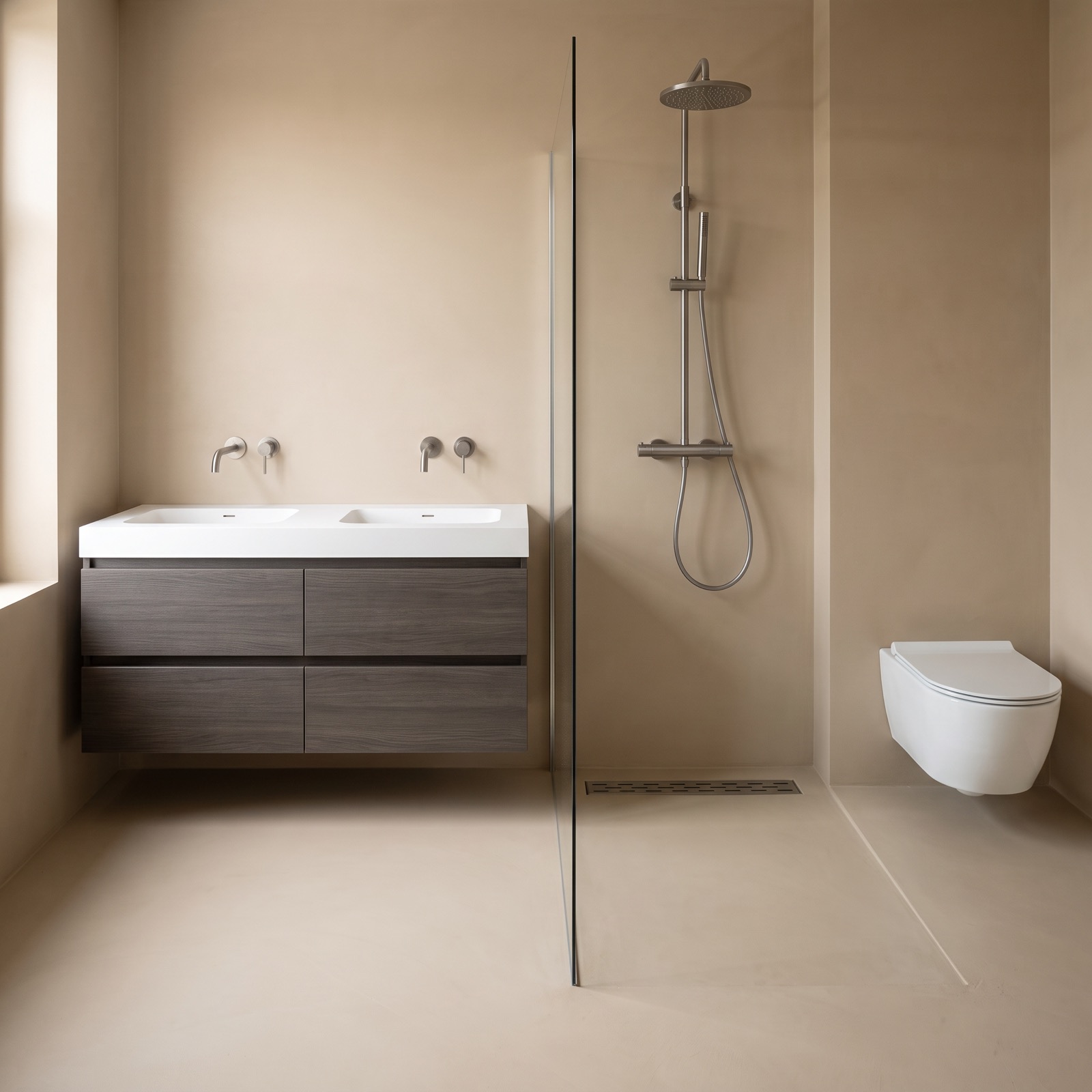 Badkamer met een grijsbruin badmeubel met een dubbele witte wastafel, een doucheset in gunmetal op de wand, een douchegoot in de vloer en een wit wandcloset